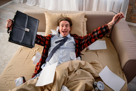 Happy adult male lying in bed and rejoicing. He is looking at camera with triumphant glance. Free from work conceptの写真素材