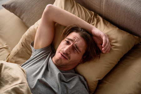 Exhausted adult male looking at camera with weary look while lying in bed at home. Top viewの写真素材