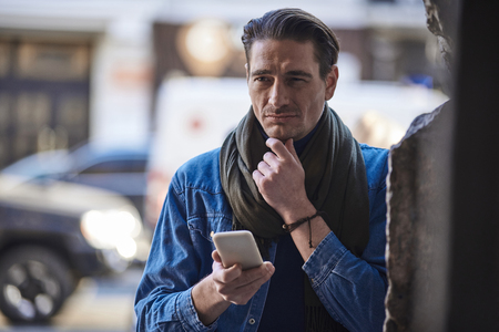 Portrait of thoughtful man typing in mobile while walking outside during sunny day. Rest conceptの写真素材