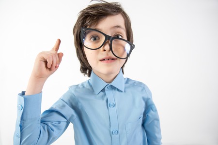 That is it. Portrait of uncombed kid with glasses aslant dreaming of making scientific breakthrough. He is holding finger up. Isolated on backgroundの写真素材