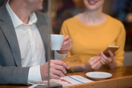 Close up man hand keeping gold card. He sitting near female in cafe. Leisure conceptの写真素材