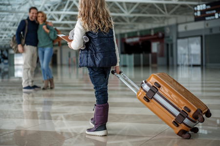 Little daughter with big case saying goodbye to parents before boarding on planeの写真素材