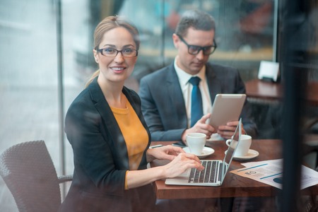 Portrait of cheerful businesswoman typing in laptop while sitting at desk. Calm colleague looking at...