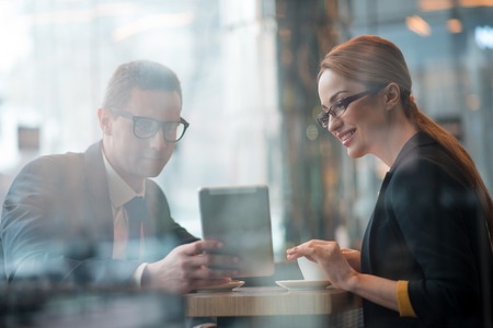 Portrait of outgoing male and happy businesswoman looking at electronic tablet. Cheerful colleagues sitting at desk. Comrades indoor. Job conceptの写真素材