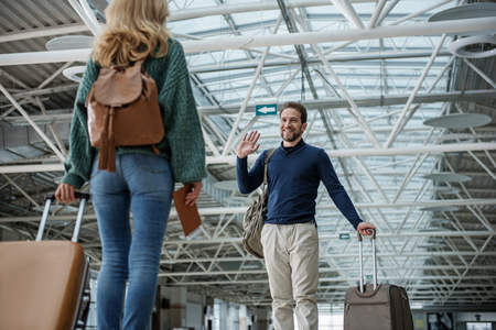 Low angle of cheerful man greeting young woman after arriving from trip. They have cases in handsの写真素材