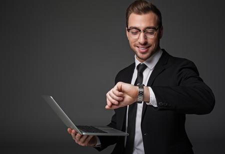Portrait of cheerful businessman looking at watch while holding notebook computer in arm. Occupation conceptの写真素材