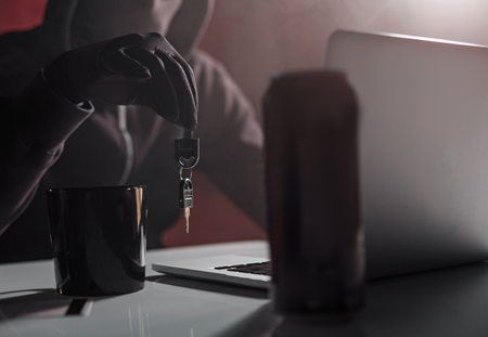 Close up male hand in black glove keeping key. He typing in notebook computer. Crime concept
