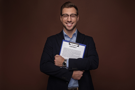 Portrait of cheerful barded businessman holding clipboard with document in arms. Profession conceptの写真素材
