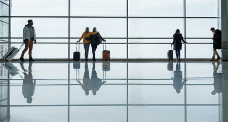 Travel concept. Full length of people are standing and looking through the window with baggage. They are waiting for flight at airport hallの写真素材