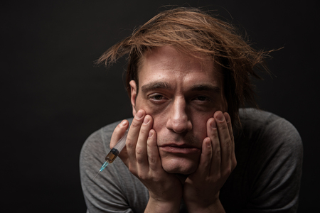 Portrait of depressed habit man with bushy hair holding syringe in his hand. Isolated on backgroundの写真素材