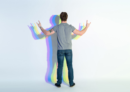 Full length young male demonstrating rock and roll sign by hands. He turning back to camera. Signifier conceptの写真素材