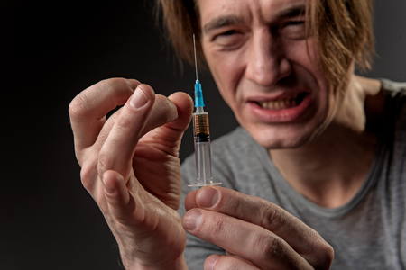 Emotional male freak preparing dose of narcotic. Focus on hands with squirt. Isolated on backgroundの写真素材