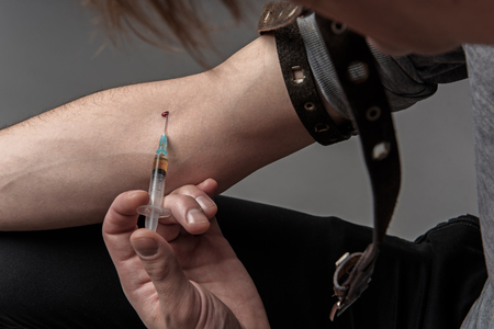 Close up of drug addicted man making a prick in the arm. Isolated on backgroundの写真素材