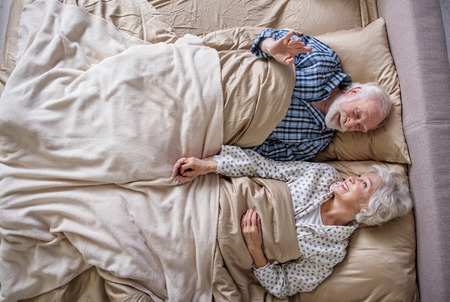 Good morning. Top view of calm senior couple waking up in the morning. They are looking at each other and holding their hands in bedroomの写真素材