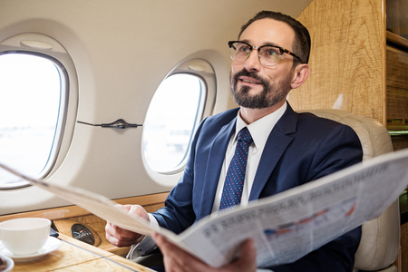 Portrait of stylish bearded male in airplane cabin holding newspaper and smilingの写真素材