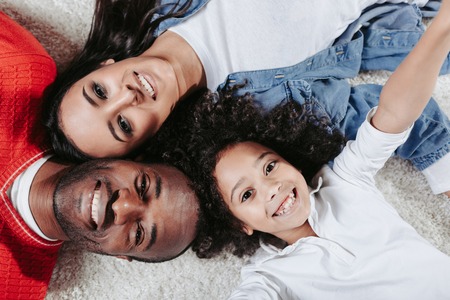 Top view portrait of parents and daughter relaxing on the warm carpet at home. They are looking at...