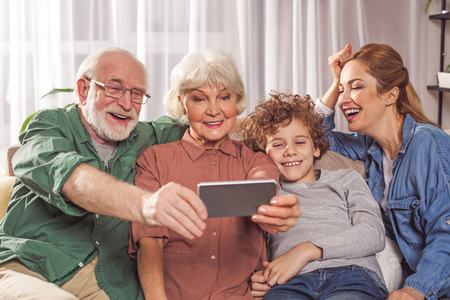 Portrait of happy grandpa, smiling child, glad grandmother and laughing mom taking selfie by mobile. Technology conceptの写真素材