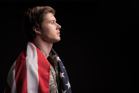 Sedate young officer standing with serious look. Flag is lying on male shoulders. Isolated on background. Copy space in right sideの写真素材
