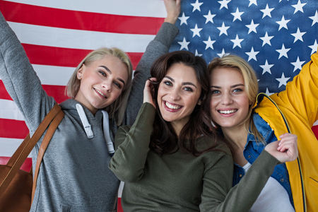 Nationalism concept. Portrait of excited women standing close. Banner of united states is on backgroundの写真素材