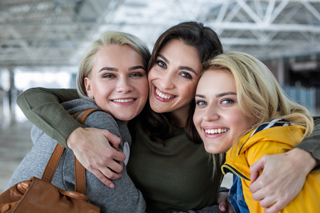 Portrait of three beautiful females hugging and looking at camera with great pleasureの写真素材