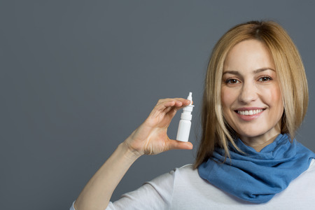 Health concept. Portrait of contented attractive woman holding nasal spray and smiling. Copy space in left side. Isolated on backgroundの写真素材