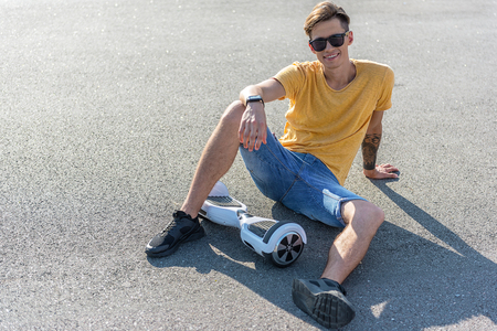 Full length portrait of cheerful teenager sitting on asphalt near gyroscope. Copy spaceの写真素材