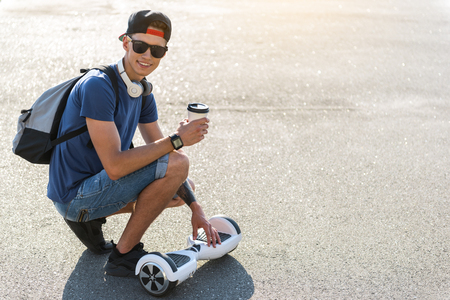 Full length portrait of outgoing boy drinking cup of delicious coffee while locating near gyroscope. Copy spaceの写真素材