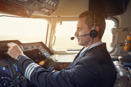 Side view serious aviator pressing buttons while talking by earphones in cockpit. Labor concept