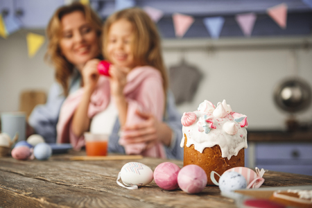 Integral elements of the holiday. Traditional pastry and colored eggs standing on wooden board. Family on backgroundの写真素材
