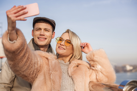 Smile. Portrait of happy joyful young couple is making selfie using smartphone while standing outdoors during their date. Selective focusの写真素材