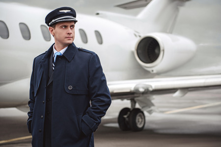 Portrait of serene young pilot putting hands in pocket. He standing opposite plane. Job conceptの写真素材