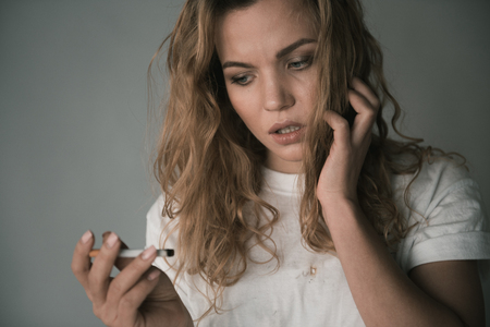 Portrait of nervous young girl looking at cigarette in her hand with discontent. Isolated on backgroundの写真素材
