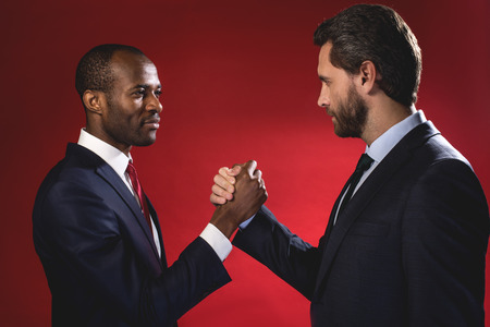 Partnership concept. Side view profile of two pleasant skilled businessmen are standing and having strong friendly handshake. They are looking at each other with smile. Isolatedの写真素材