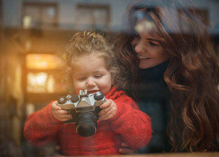 Well done. Curious girl is looking into the camera lens and smiling. Woman is embracing child with...