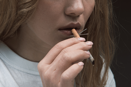 Injury concept. Close up of female hand bringing to mouth prickly ciggy. Isolated on backgroundの写真素材