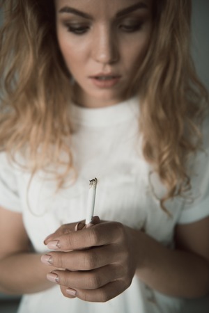 Nicotine addicted woman looking at ciggy end with despite. Focus on hands keeping cigarette. Isolated on backgroundの写真素材