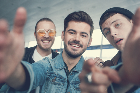 Portrait of happy male friends taking selfie while keeping camera in hands indoor. Entertainment...
