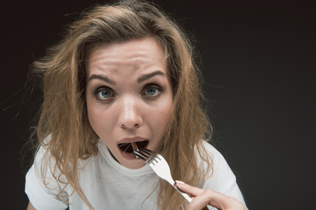 Portrait of woman with shocked facial expression putting into the mouth prickly tobacco product. Copy space in right side. Isolated on backgroundの写真素材