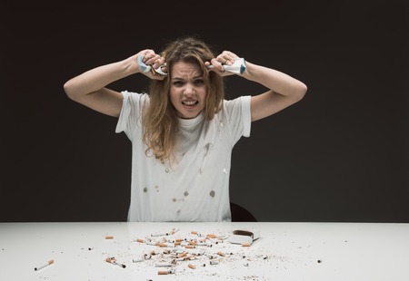 Waist up portrait of untidy stressed female squeezing cigarette packs expressing rage. Isolated on backgroundの写真素材