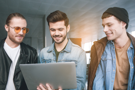 Outgoing male friends looking at notebook computer while standing in airport. Technology conceptの写真素材