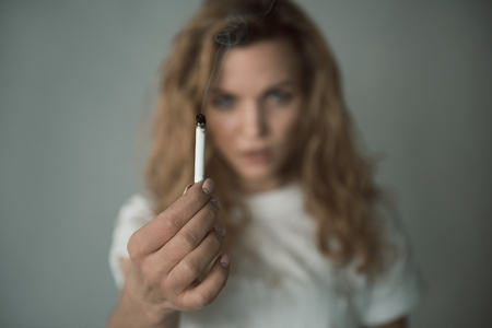 Portrait of unhappy woman demonstrating burning ciggy. Focus on coffin nail. Isolated on backgroundの写真素材