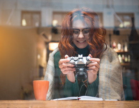 Good memories. Waist up portrait of happy young woman looking at photographs on camera screen. She is smiling while relaxing in cozy cafeteriaの写真素材