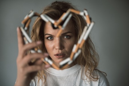 Portrait of quiet lady looking through heart made of cigarettes. Focus on face. Isolated on backgroundの写真素材