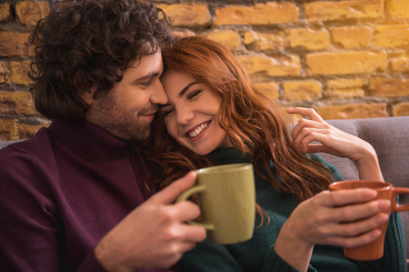 Portrait of relaxed young man and woman embracing and laughing. They are drinking cup of coffee with enjoymentの写真素材