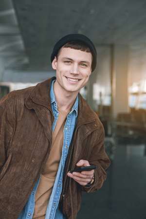 Portrait of beaming man typing in mobile while standing in airport. Technology and trip conceptの写真素材