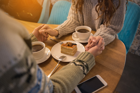 Top view close up of loving couple holding hands while sitting in restaurant. Cups of coffee and piece of cake on tableの写真素材