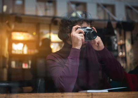 Calm young man is photographing street while sitting near window in cafe. Copy spaceの写真素材