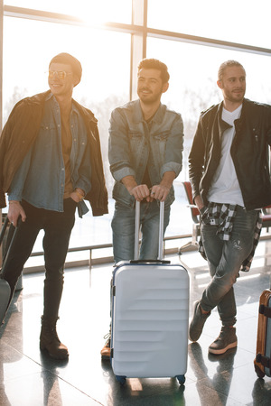 Full length portrait of cheerful comrades standing with baggages in airport. Journey conceptの写真素材