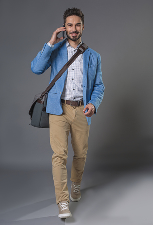 Full length portrait of going handsome guy with briefcase talking on phone and smilingの写真素材