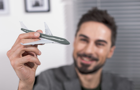 Focus on miniature plane in male hand. Glad man on background. Dreaming about travel conceptの写真素材